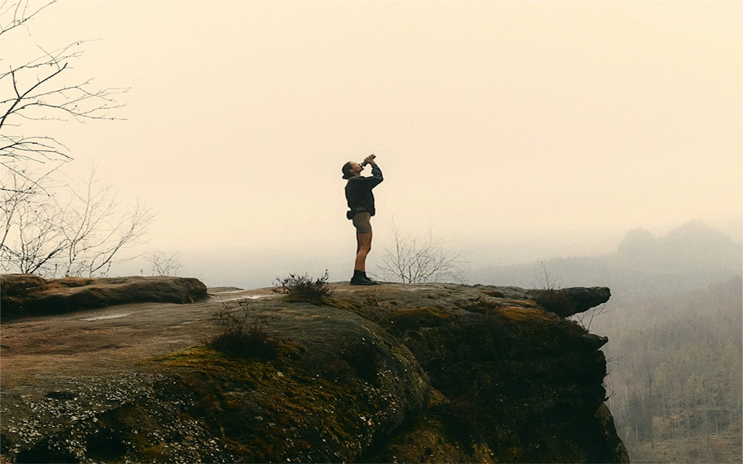 Hiker drinking from a bottle on a misty rock ledge