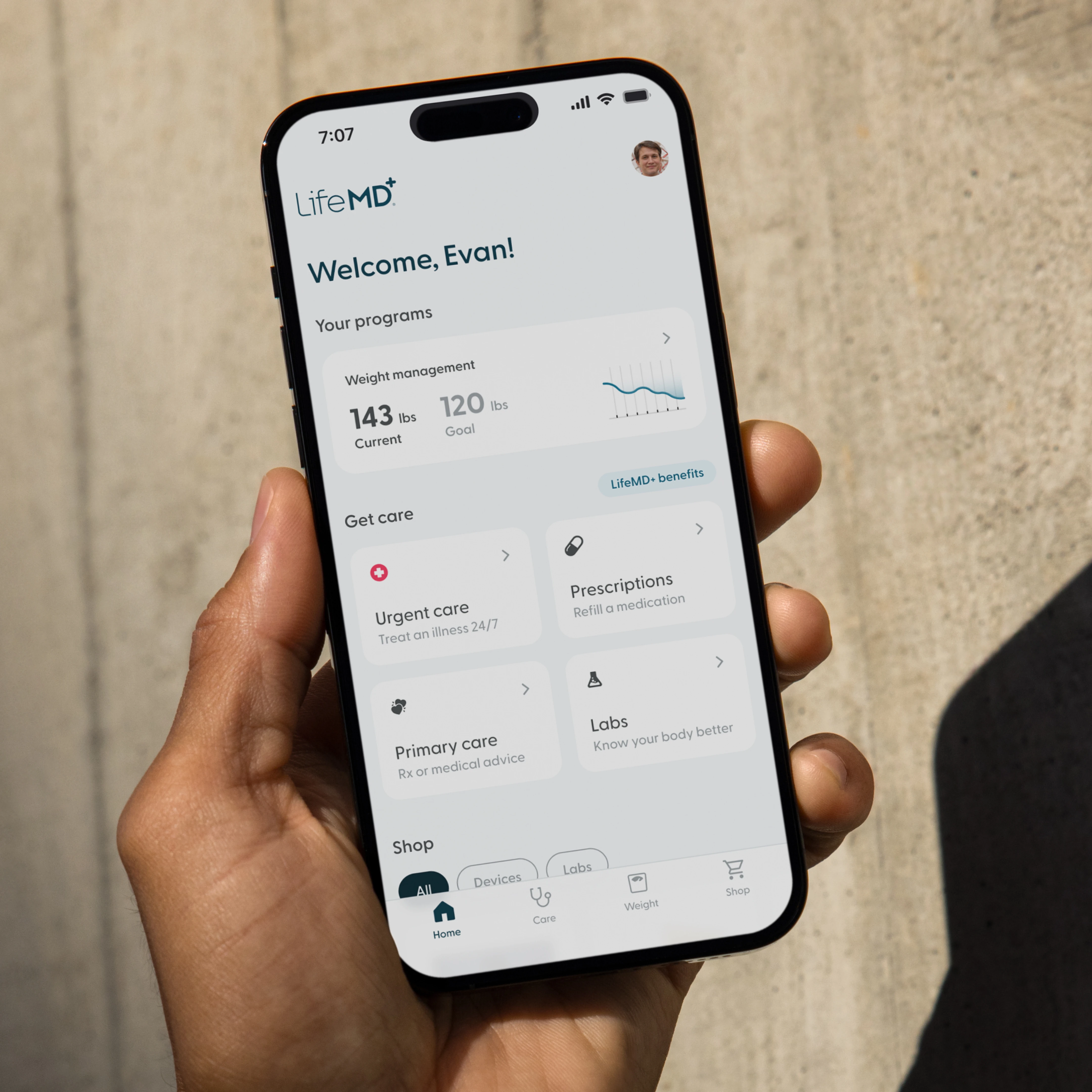 Hand holding an iPhone with the LifeMD home screen, programs and care options